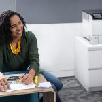 Xerox® VersaLink® C620 Drucker in einem Büro Lächelnde Frau in einem Büro neben dem Xerox® VersaLink® C620 Farbdrucker